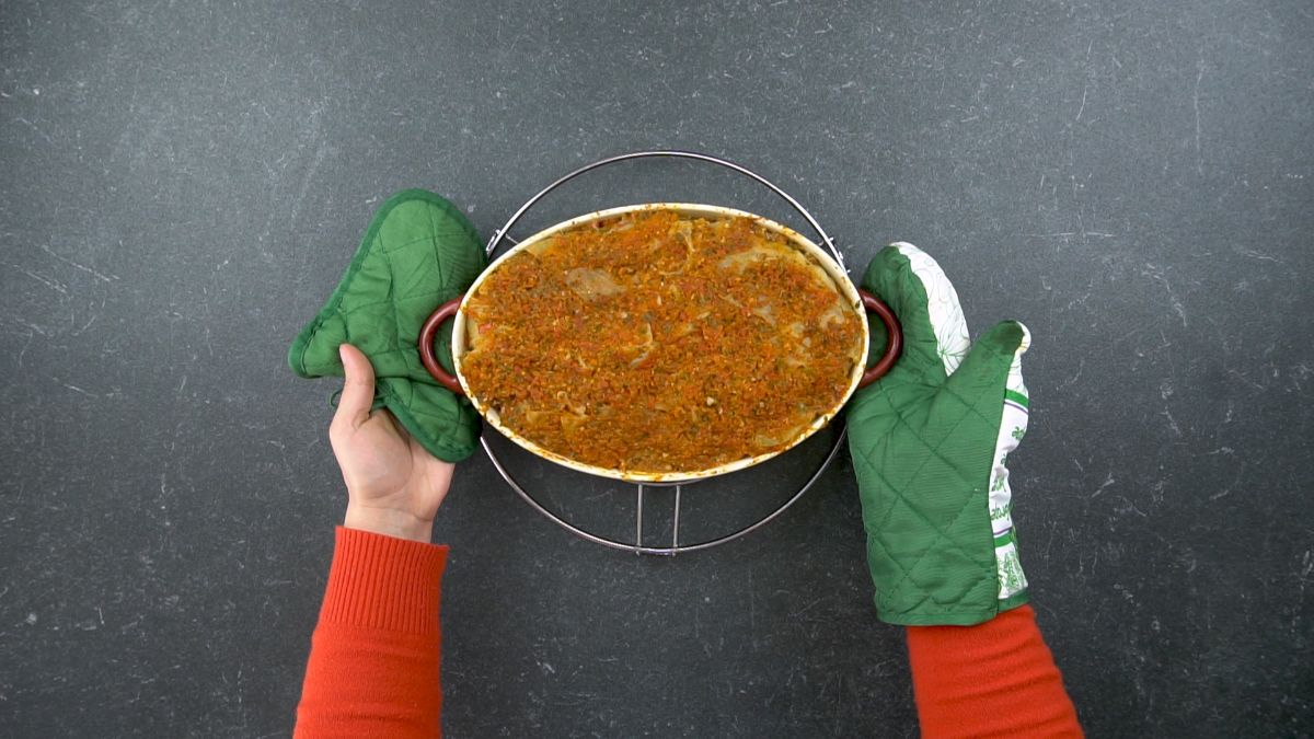 hand in green oven mits putting casserole dish onto trivet