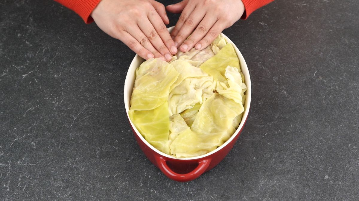 hands putting cabbage leaves over top of casserole