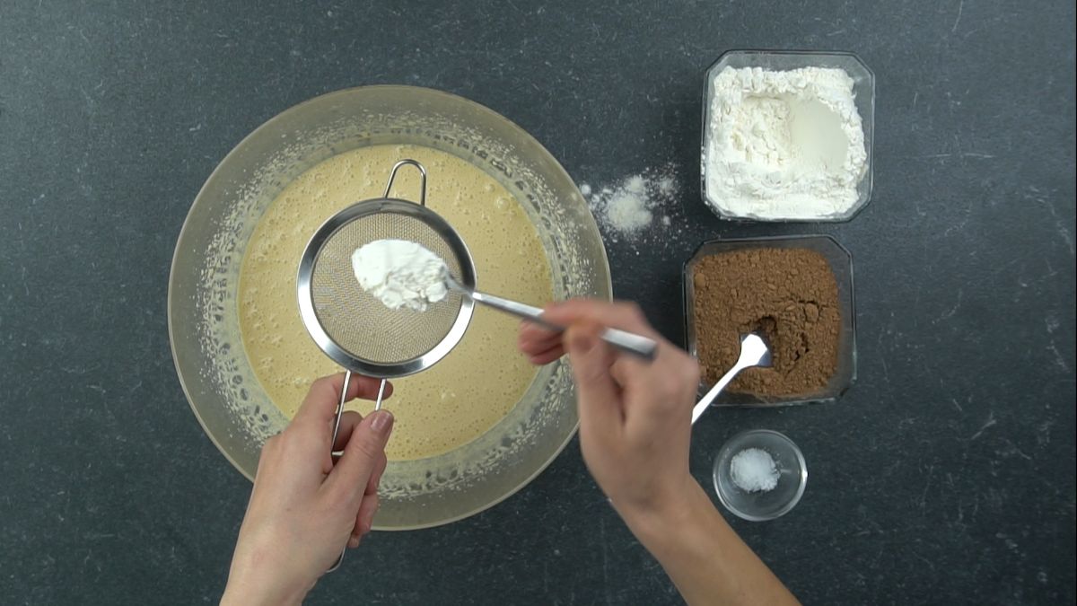 hand sifting flour into bowl of yellow egg mixture
