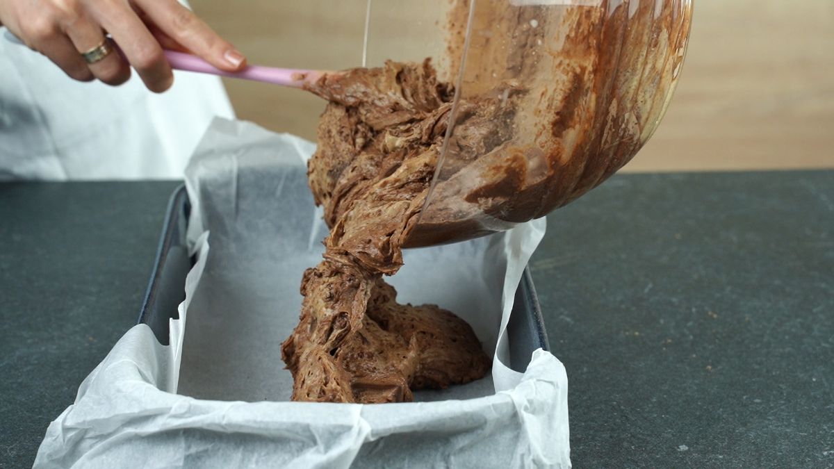 spatula scooping brownie batter into lined baking dish