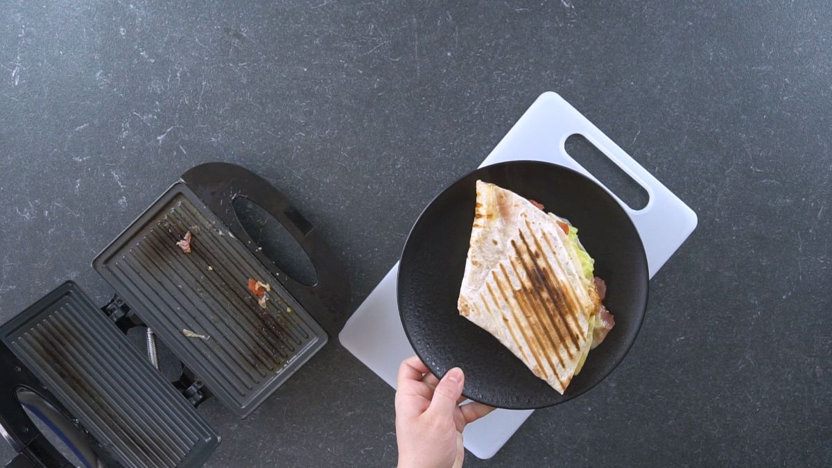 hand holding black plate with tortilla wrap next to sandwich maker