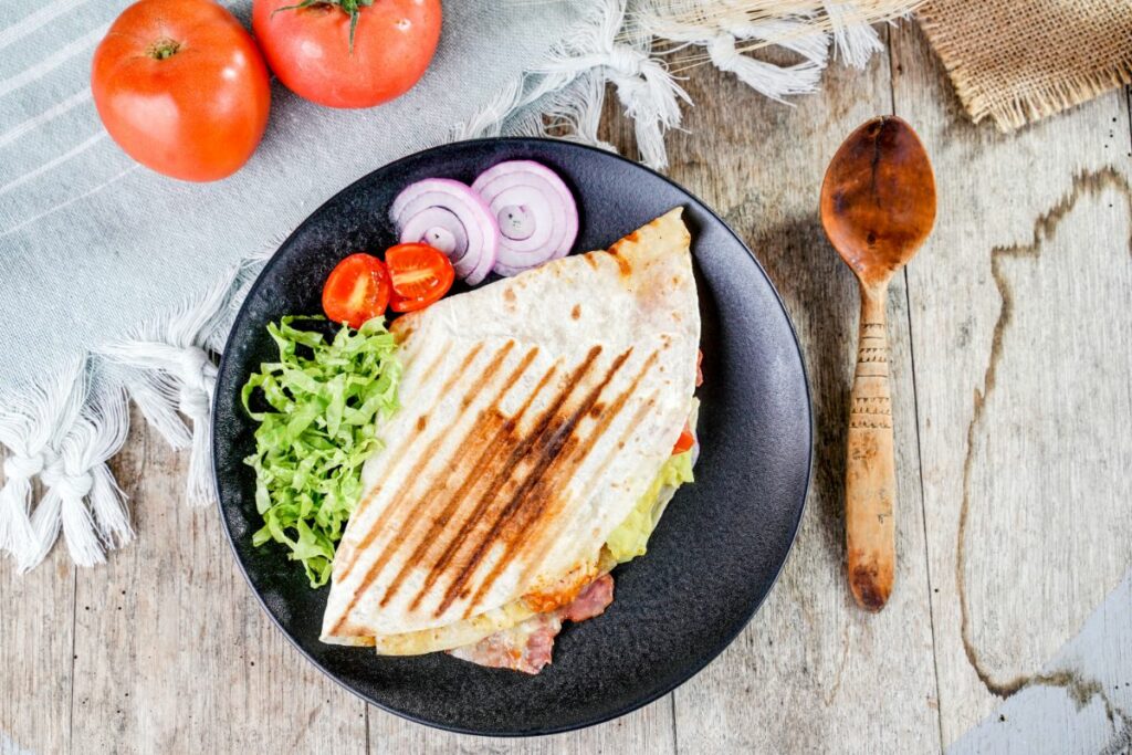 image looking down at black plate of tortilla wrap with salad on wood table by wood spoon