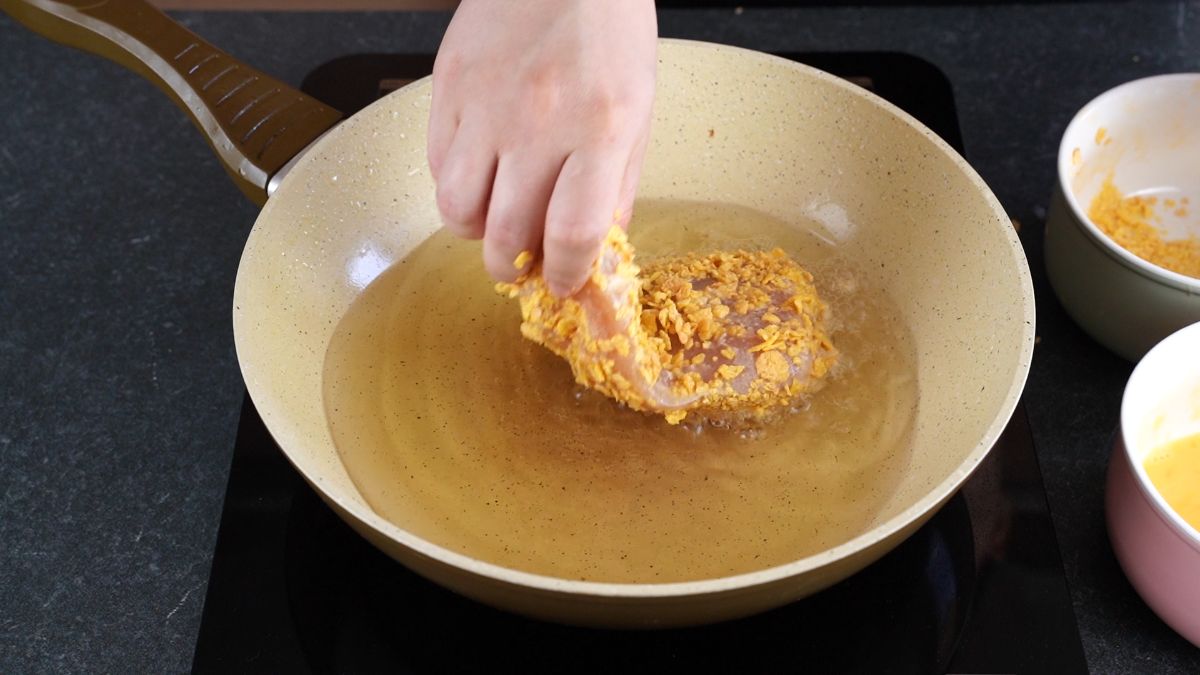 hand putting breaded chicken cutlet into pan of hot oil