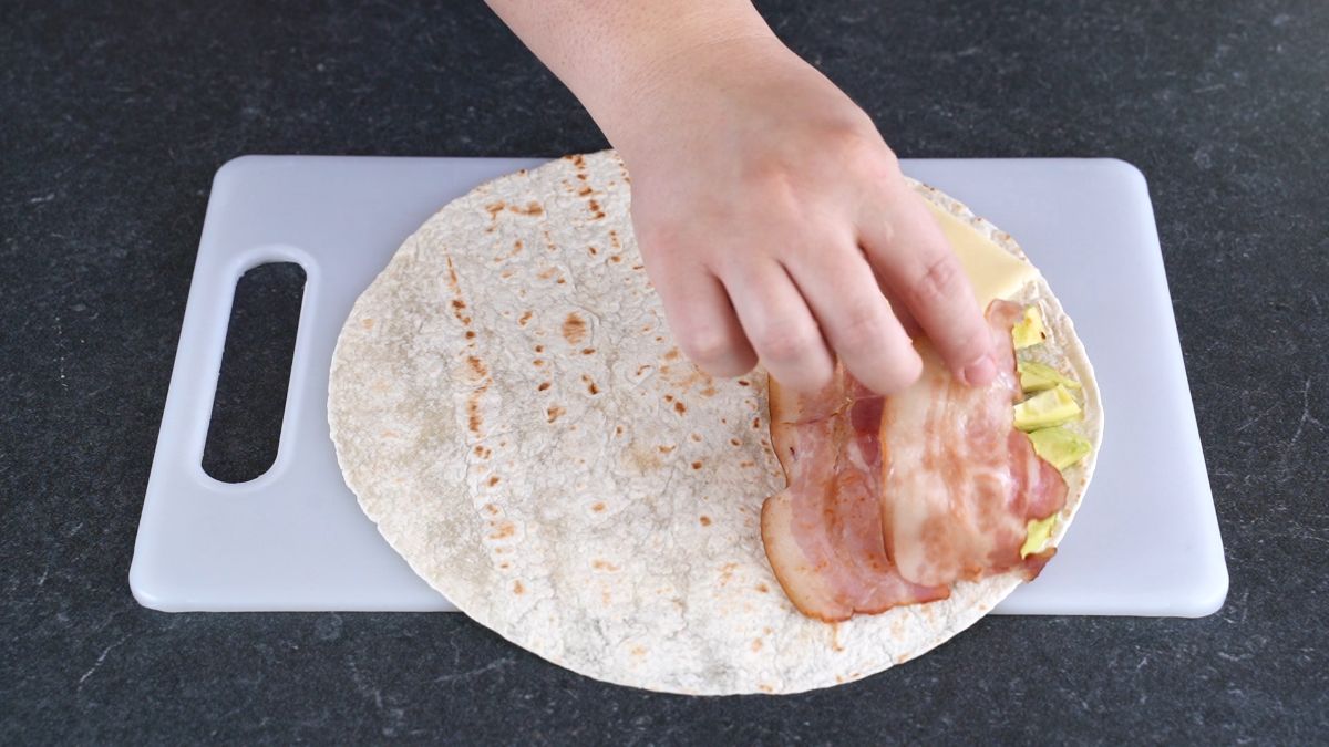 hand putting bacon on tortilla