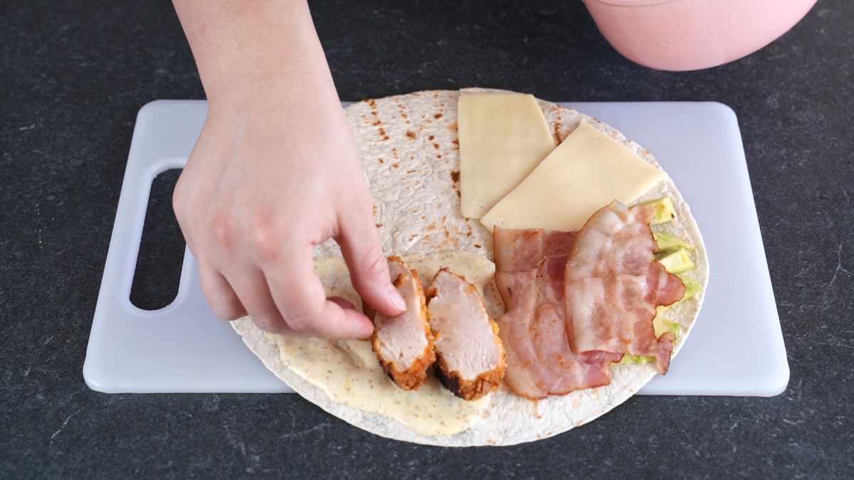 hand placing chicken slices on tortilla