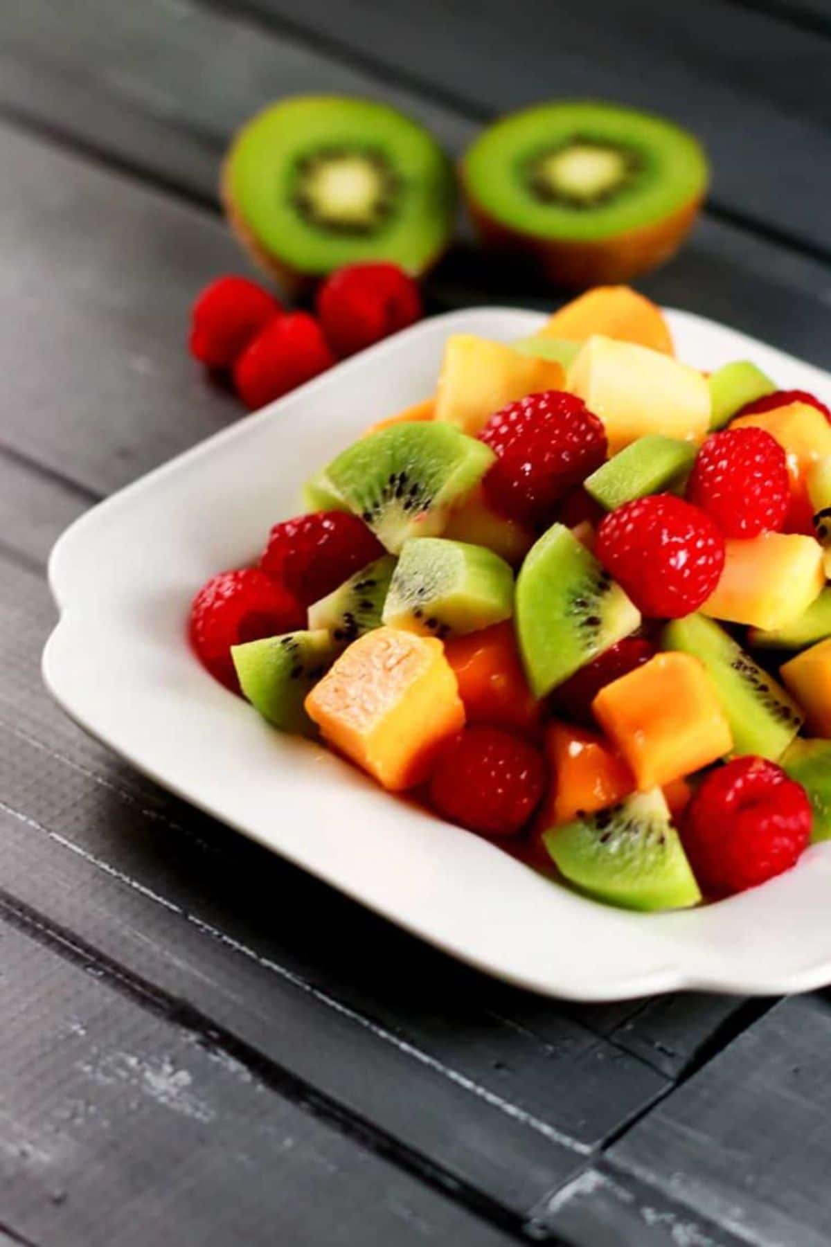 white square bowl on table with kiwi mango and raspberries