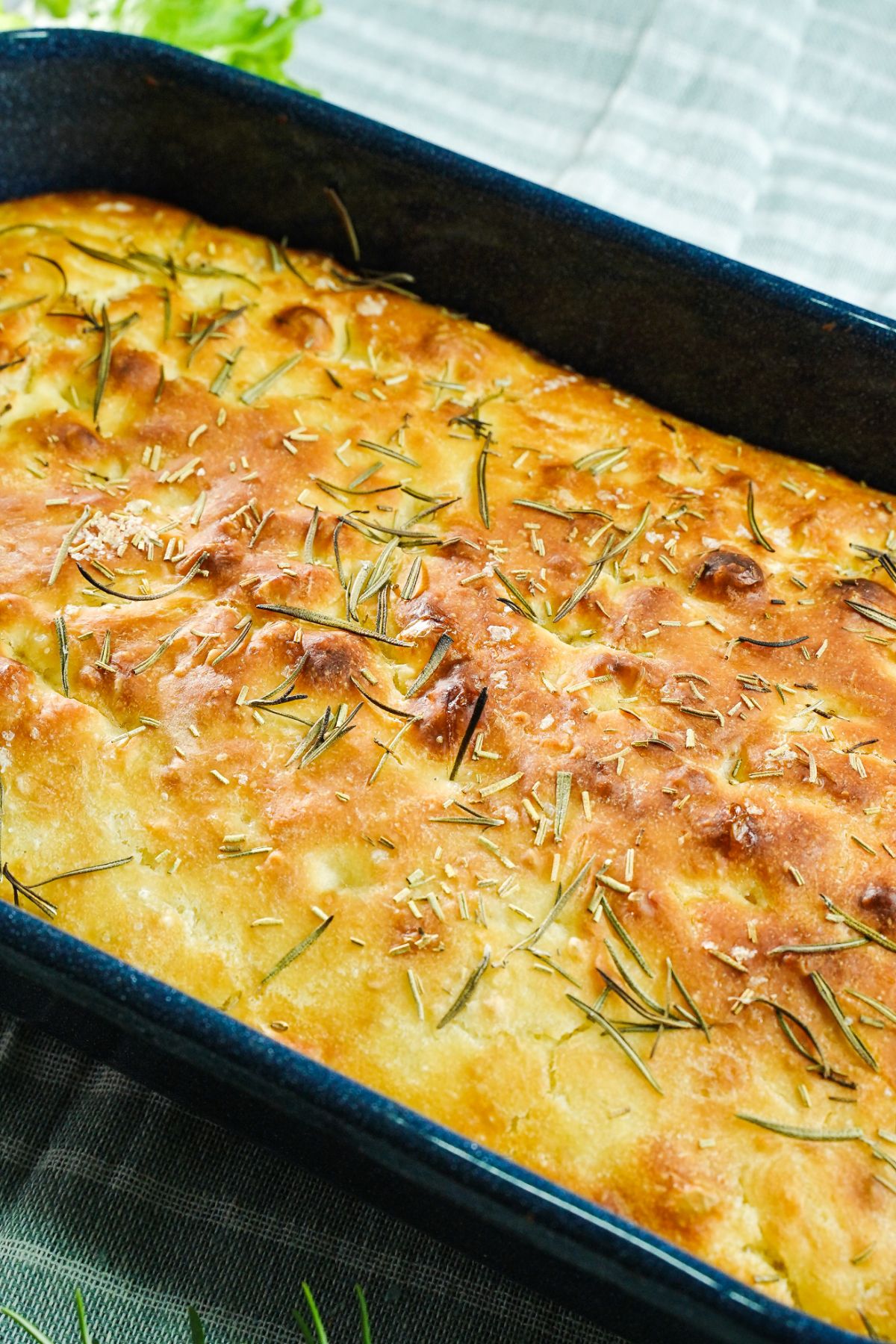 close up image of focaccia with rosemary on top in black pan