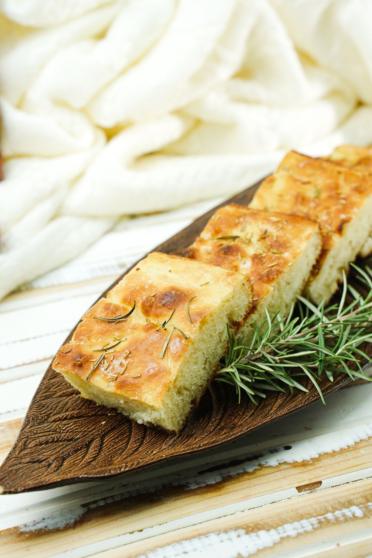 brown platter holding sliced bread with rosemary sprig on the side