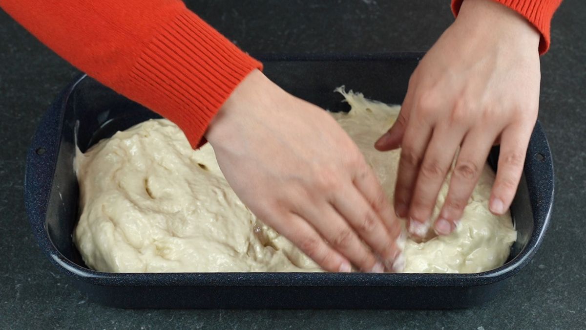 hands punching down dough in baking dish