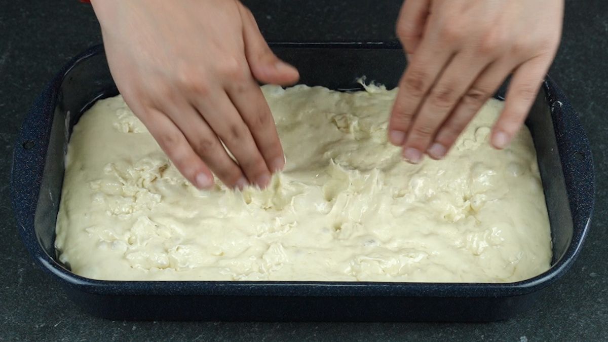 hands making divots in top of bread dough