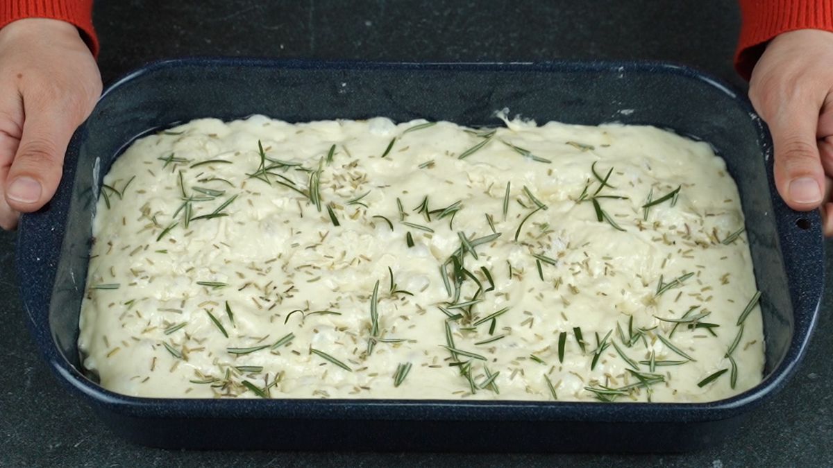 rosemary sprinkled over the top of raw dough in black pan