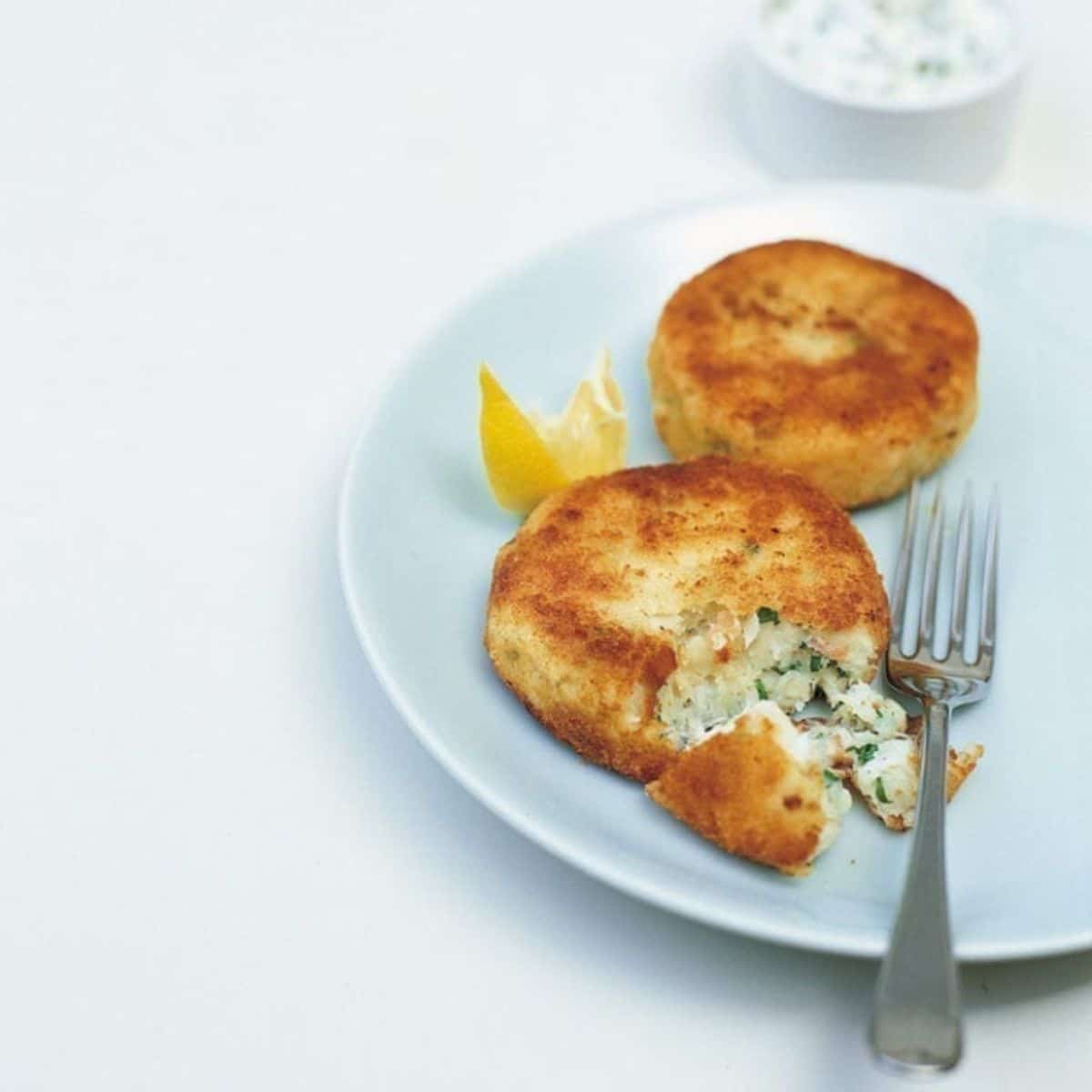 fish cakes on light blue saucer with fork on white table