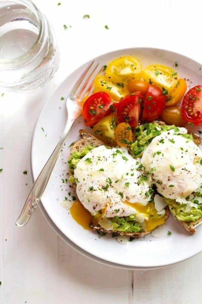 two eggs on top of avocado toast next to heirloom tomatoes
