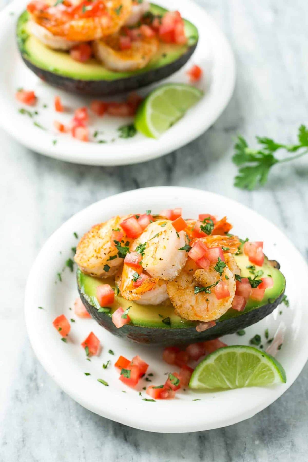 shrimp on top of half avocado on plate with pico de gallo and lime