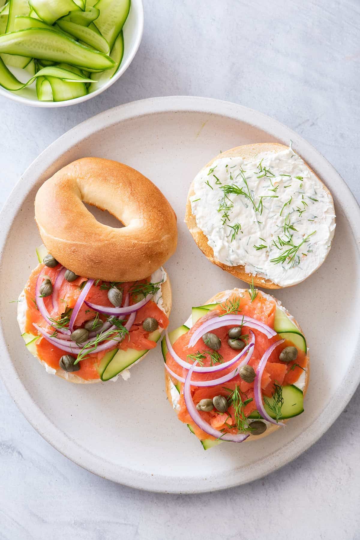 two bagels with salmon and capers on white round plate