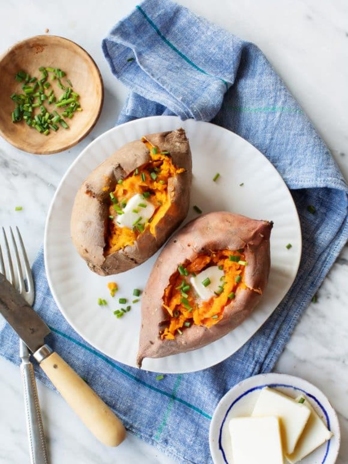 two baked sweet potatoes on round white plate with blue napkins underneath