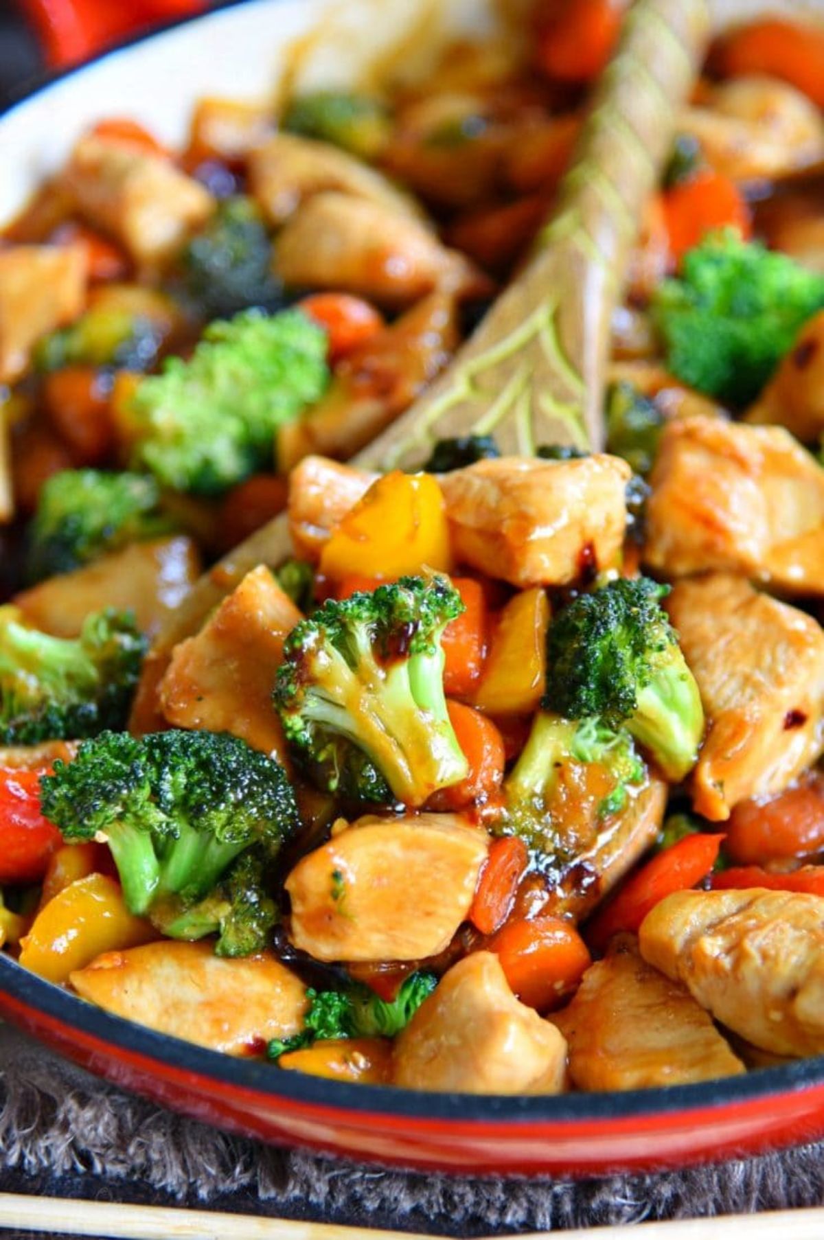 wooden spoon in red skillet of chicken and broccoli stir fry