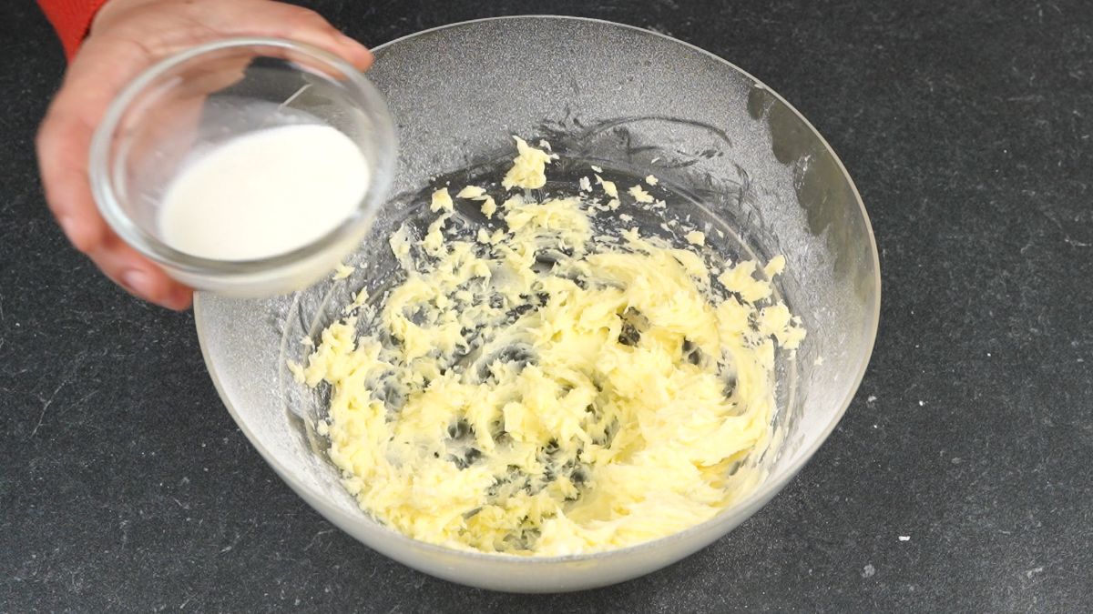 glass bowl of creamed butter with small bowl of milk held above