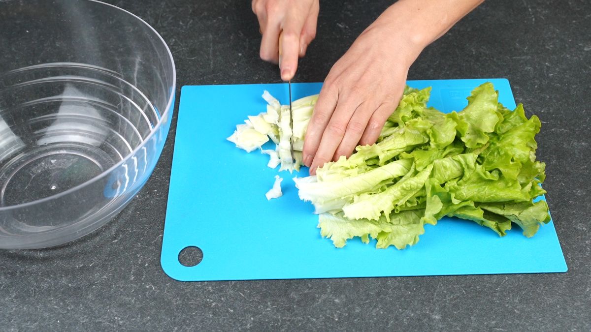 salad being cut with knife on blue cutting board