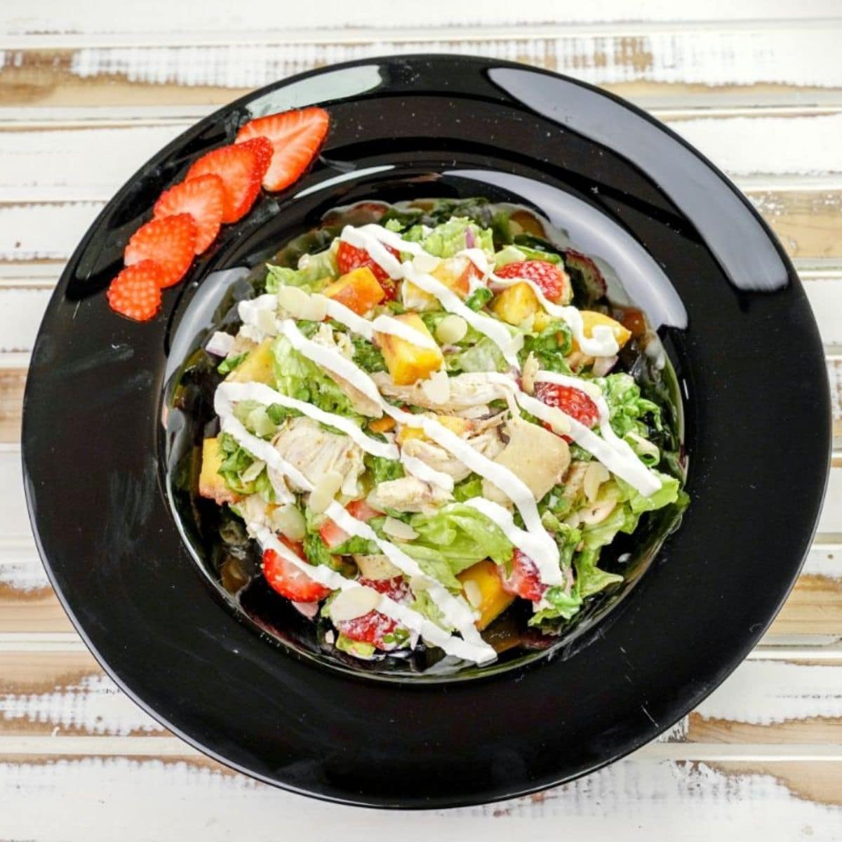 round black plate with salad and strawberries on wood table