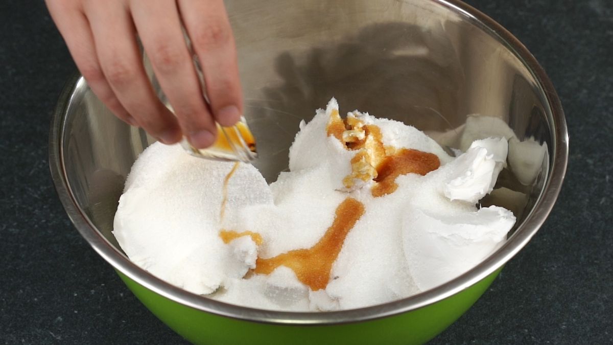 hand pouring vanilla extract into bowl with cream cheese