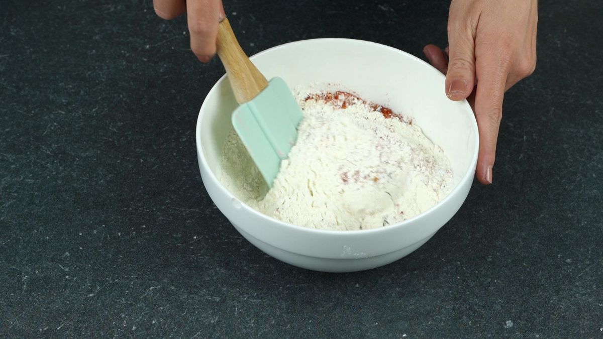 blue spatula stirring flour and spices in white bowl