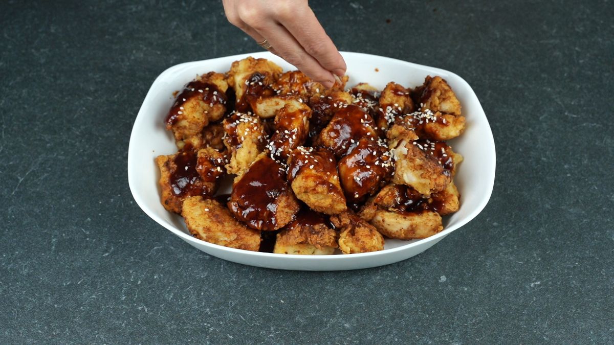 hand sprinkling sesame seeds on sauced d fried chicken pieces