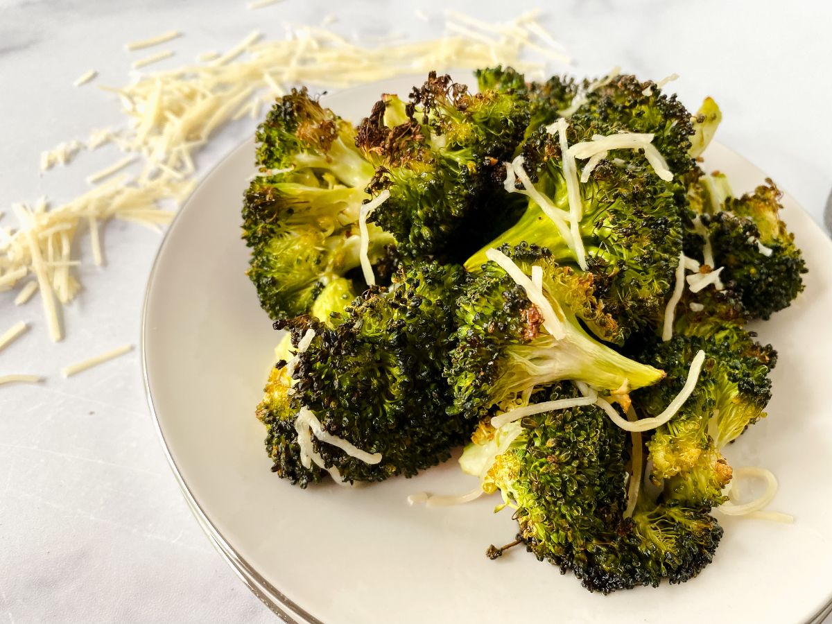 white plate of broccoli on marble table with parmesan shreds