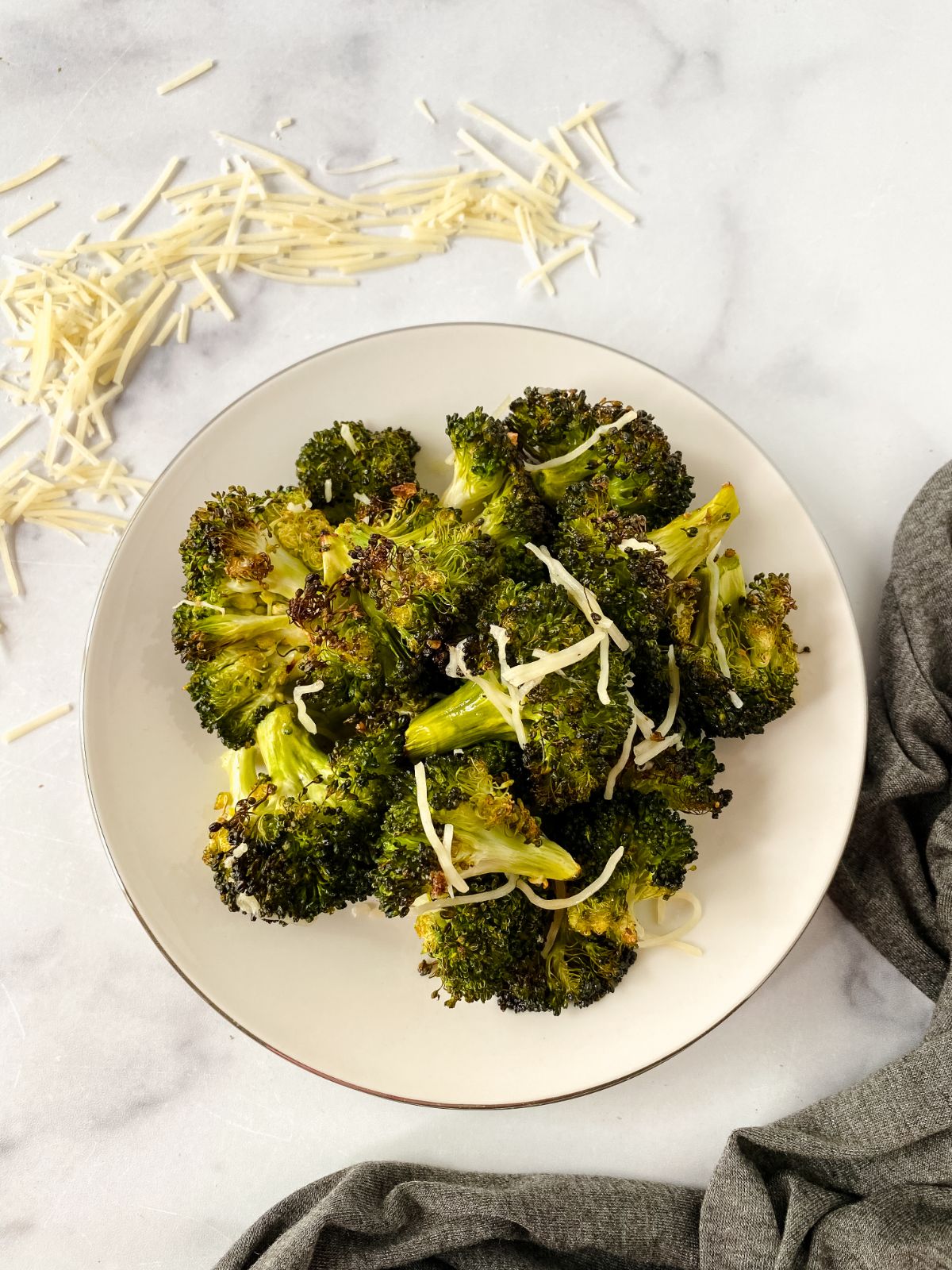 broccoli with parmesan on white plate sitting on marble table by grey napkin