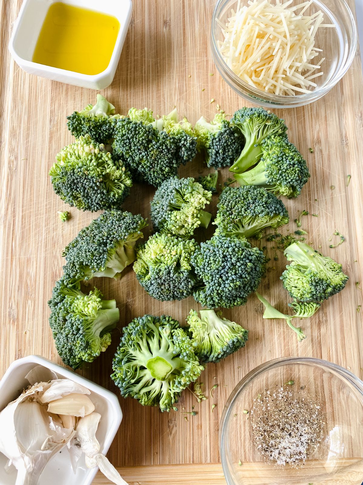 broccoli on cutting board with bowls of spices and cheese on side