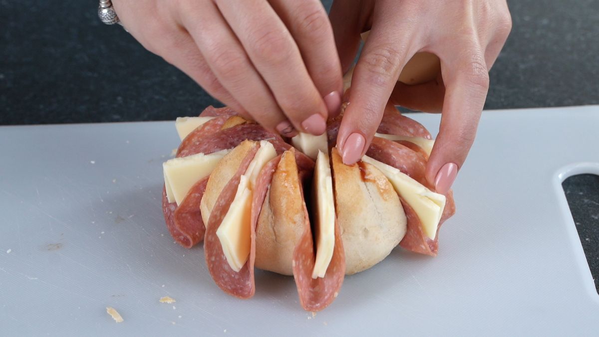 hand putting cheese into bun with pepperoni