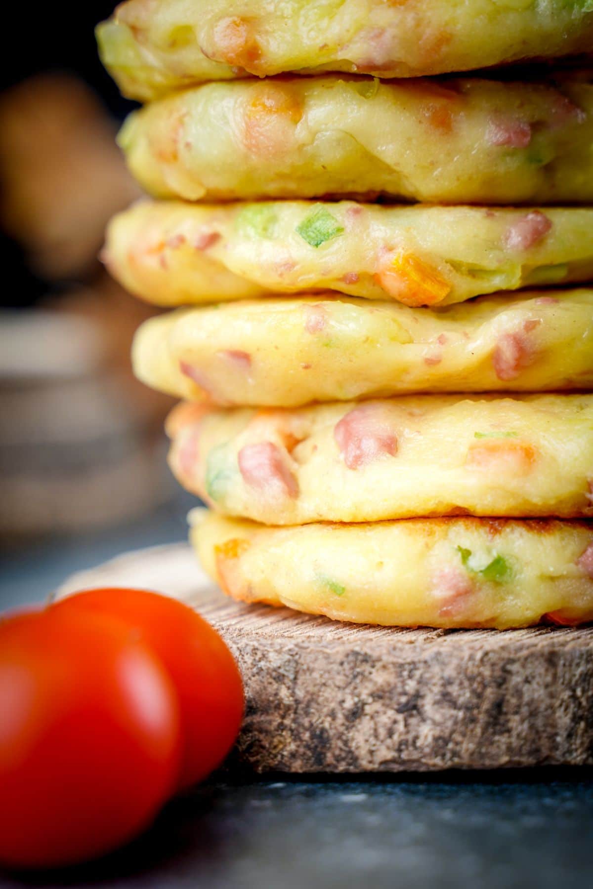 stack of [potato cakes sitting on wood disc by cherry tomato