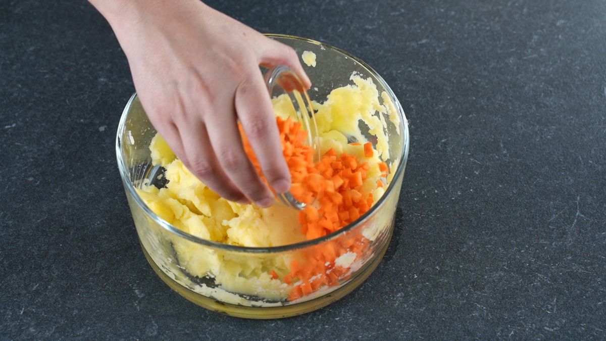 carrots being added to potatoes in glass bowl
