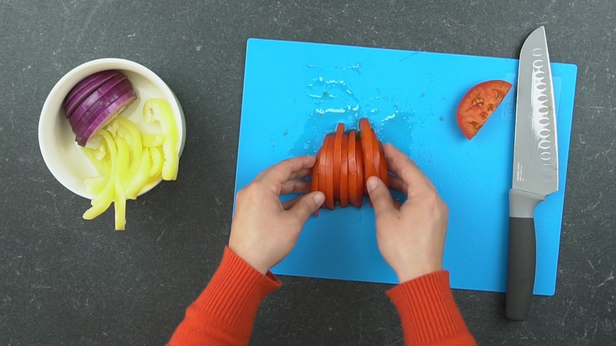 hand picking up sliced tomatoes on blue cutting board