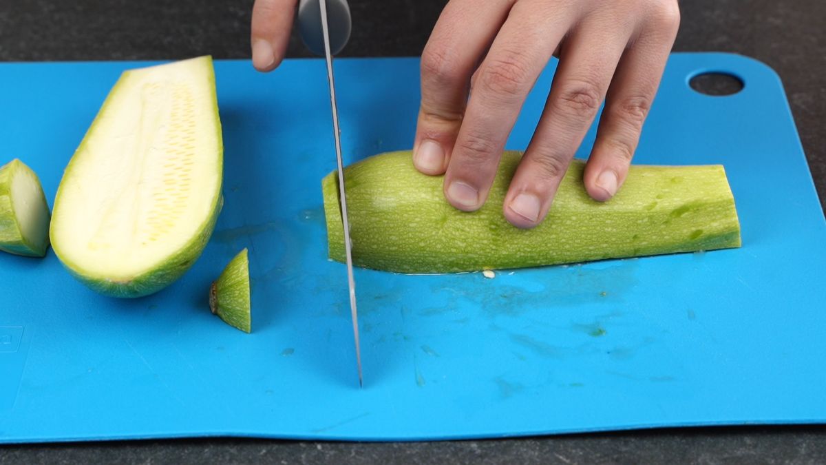 hand holding knife slicing zucchini