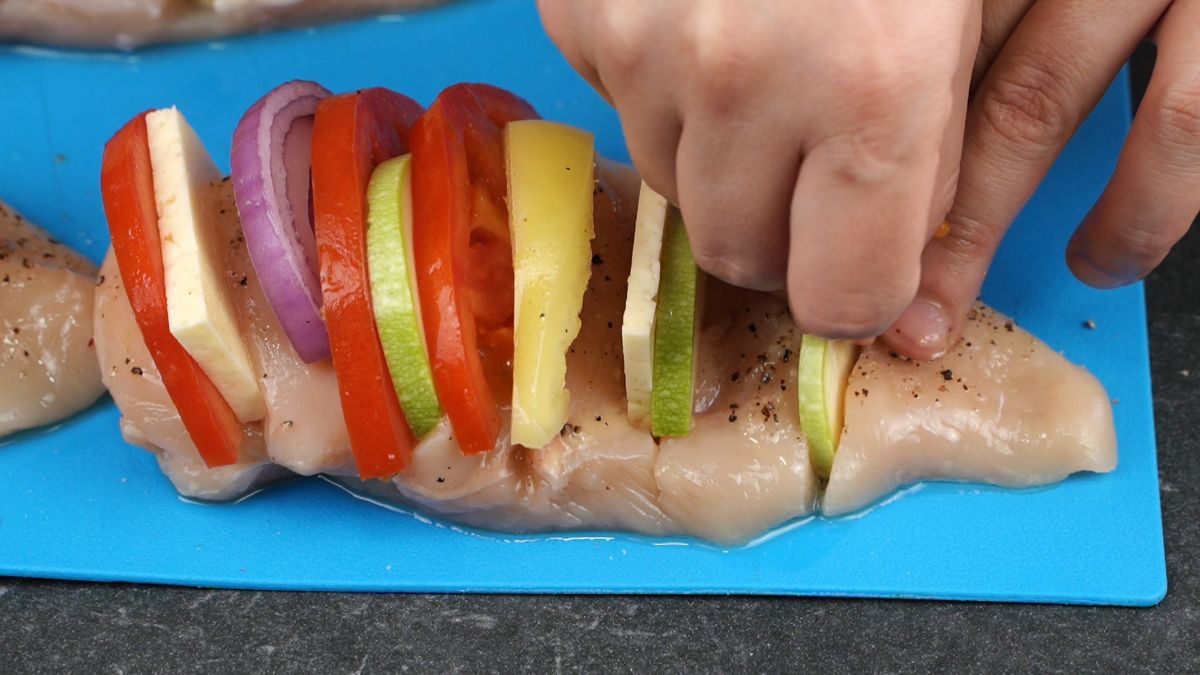 hand stuffing vegetables into chicken breast