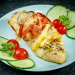 stuffed chicken breast on light blue plate next to tomatoes and cucumber slices