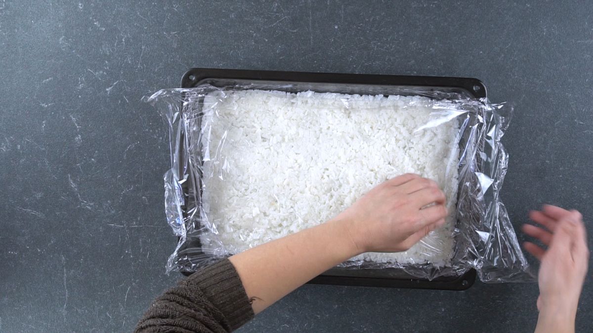 rice in baking sheet being covered by plastic wrap