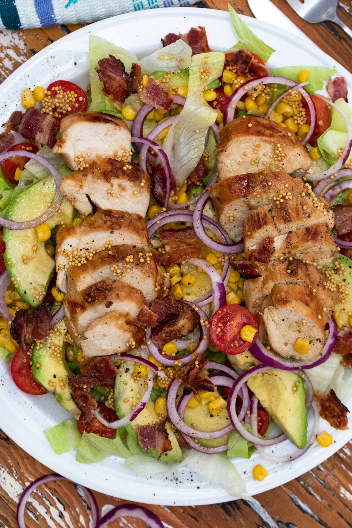 slicd chicken breasts on salad greens with onion tomato and avocado on white plate