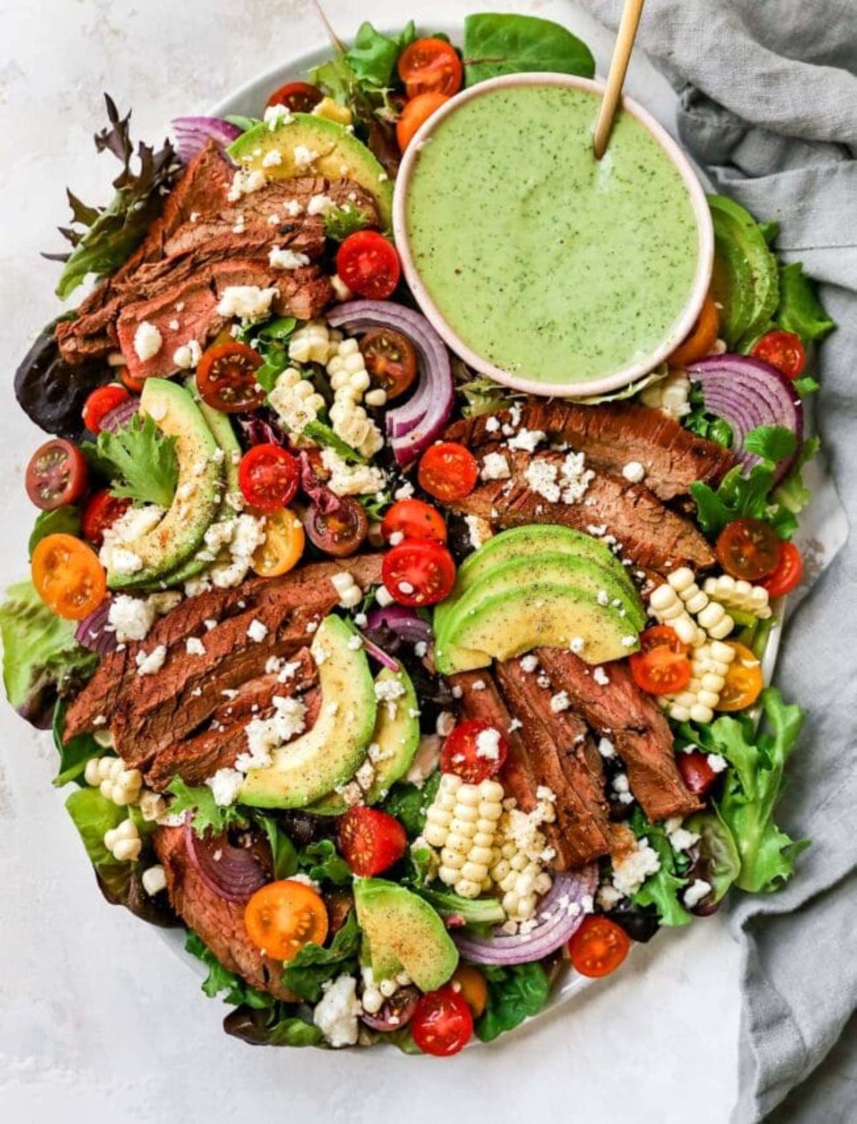 steak salad with white bowl of avocado dressing