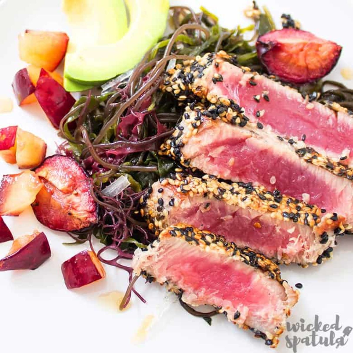 sliced tuna on top of seaweed on white plate
