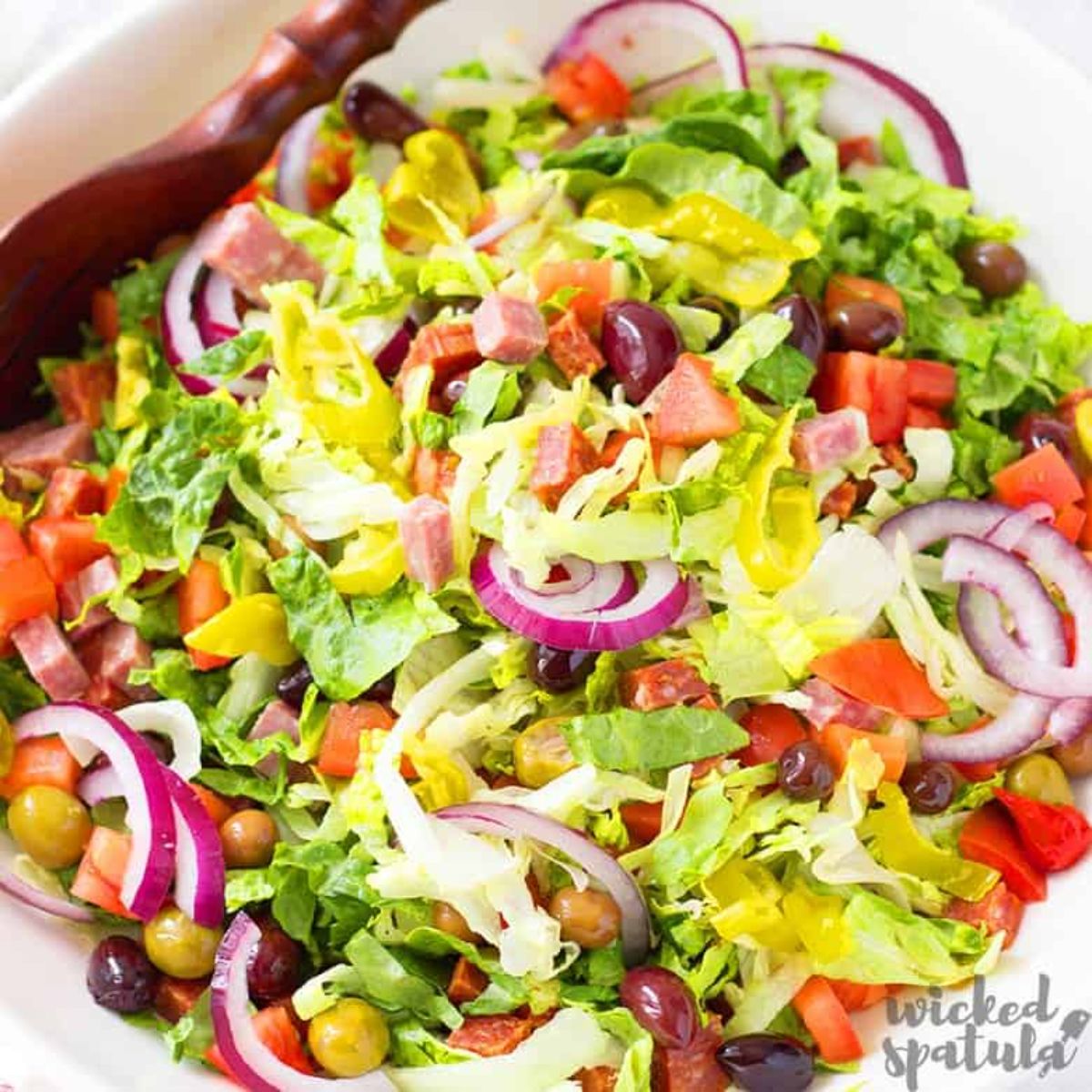 chopped italian salad with dark wood spoon in white bowl