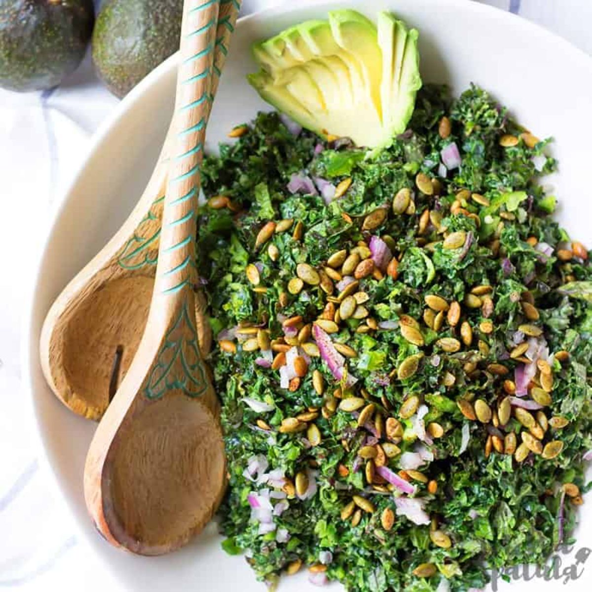 white bowl of kale salad with wooden spoons