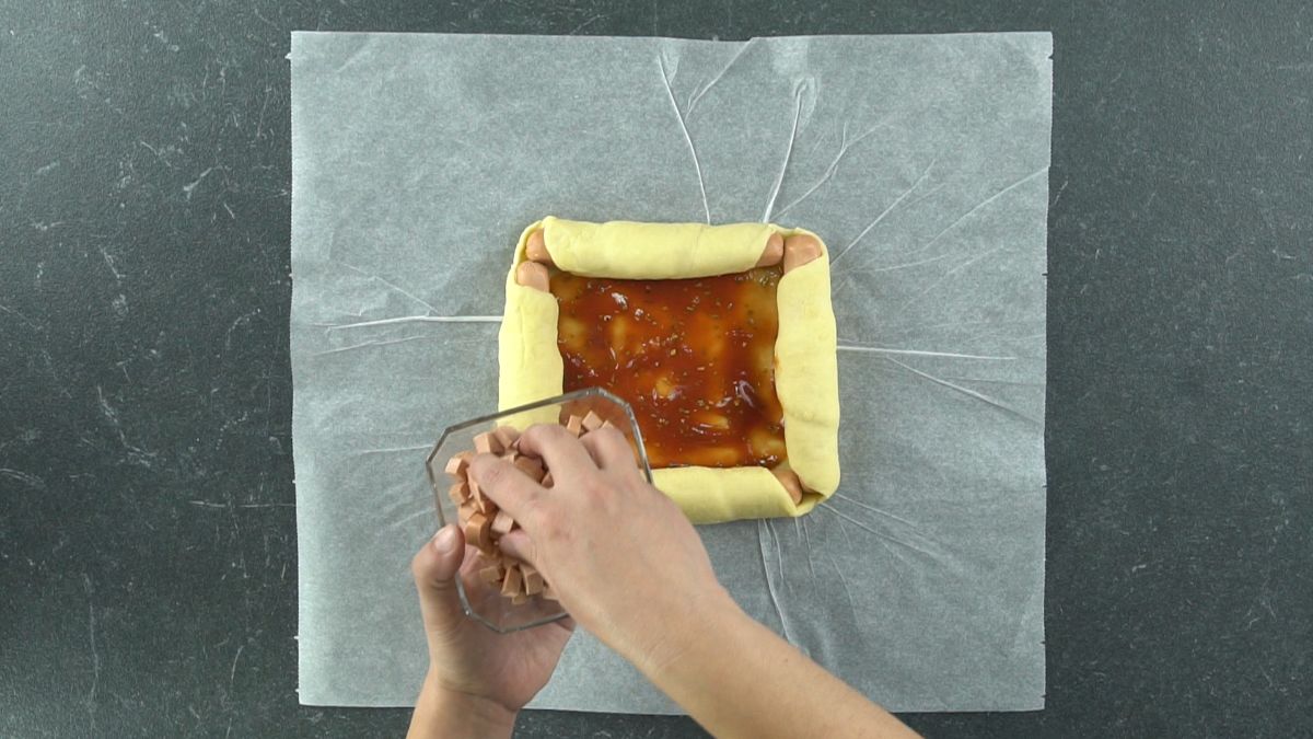hand holding sausage above pizza sauce in middle of dough