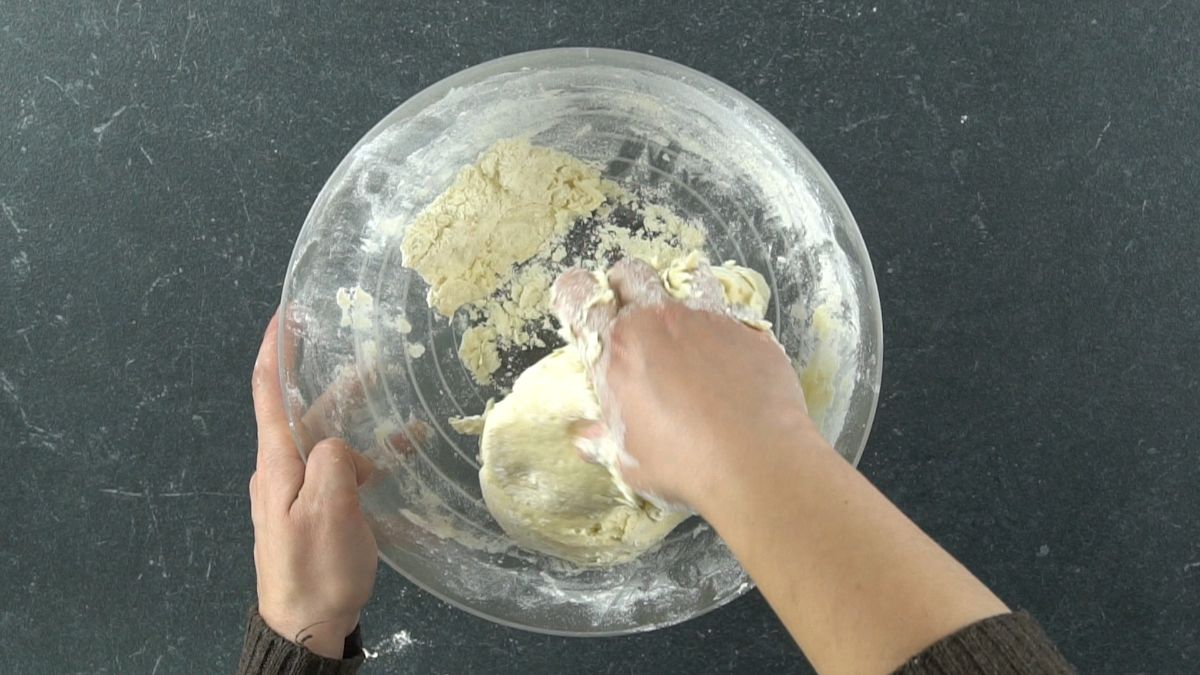 hand kneading dough in glass bowl