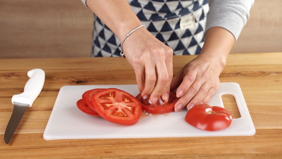hand using small glass bowl to remove inside of tomato ring
