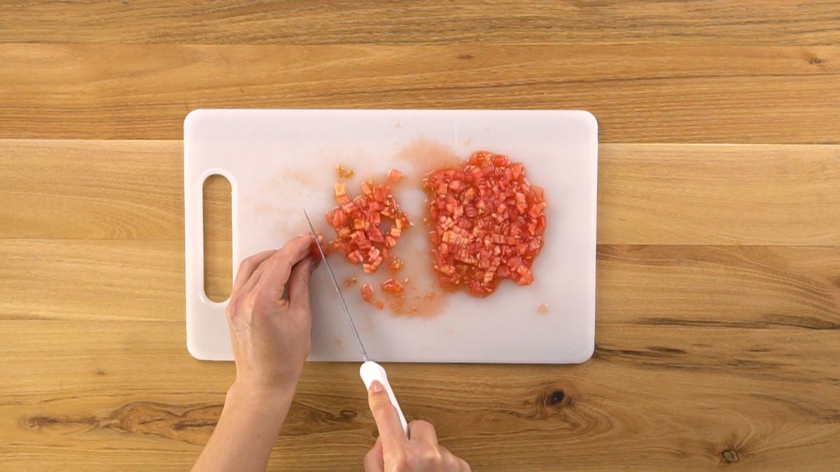 hand chopping tomatoes on white cutting board sitting on wood table