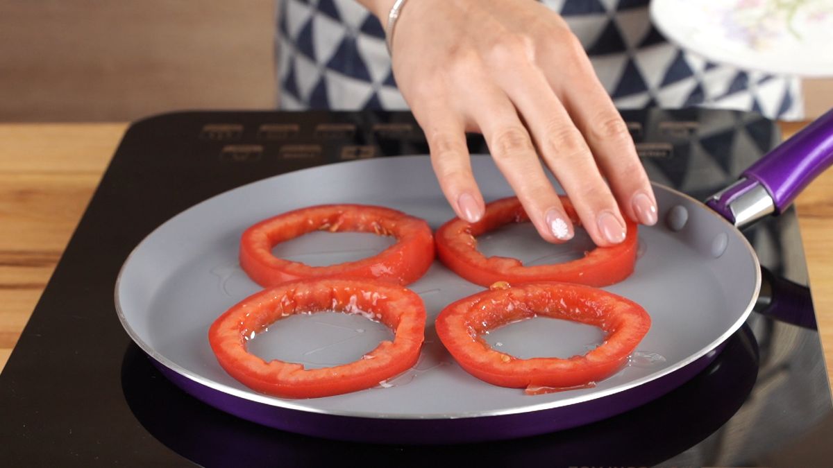 hand placing tomato rings onto skillet on black hot plate