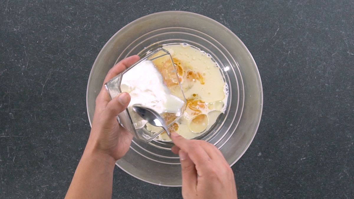 hand spooning sour cream into glass bowl of eggs