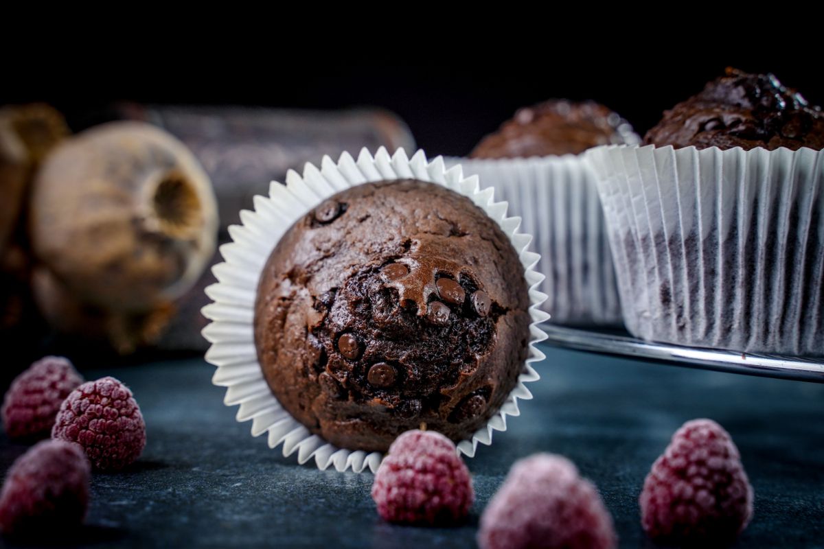 muffin with chocolate chips in white liner laying on its side on black table